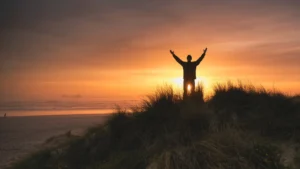 man holding high up in facing sunset feeling blissful